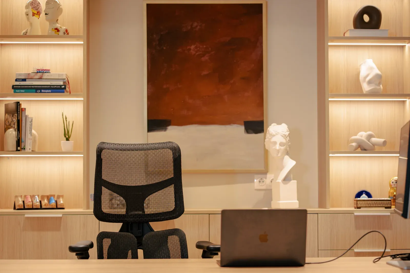 Despacho de la consulta en LĀR CLINIC, con estanterías iluminadas, una escultura y una mesa de trabajo