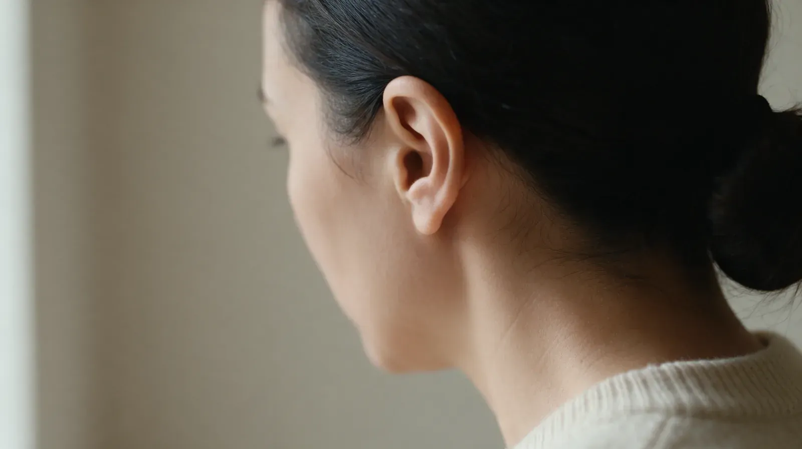 Adult woman seen from behind with her hair tied up, showing her left ear in natural light
